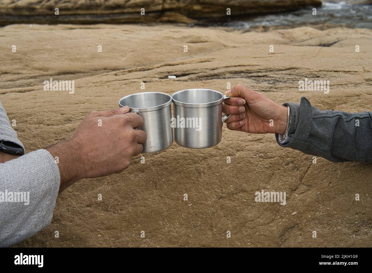 Un paio di mani che uniscono le coppe d'argento sulla riva del mare Foto Stock