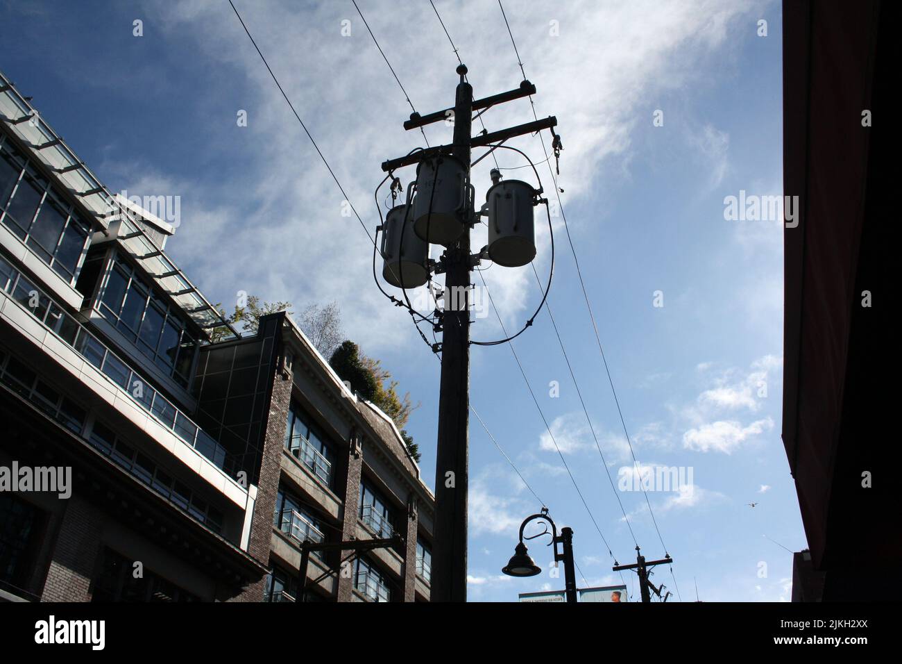 Una silhouette di palo contro un cielo blu con nuvole bianche e un edificio sul lato sinistro Foto Stock