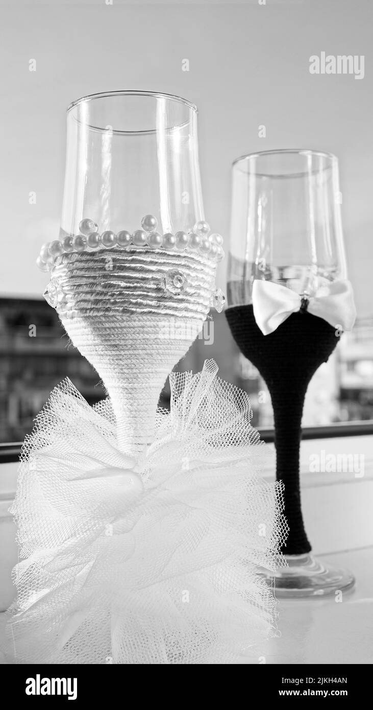 Una foto in scala di grigi di un paio di bicchieri da champagne con design a tema sposa e sposo Foto Stock