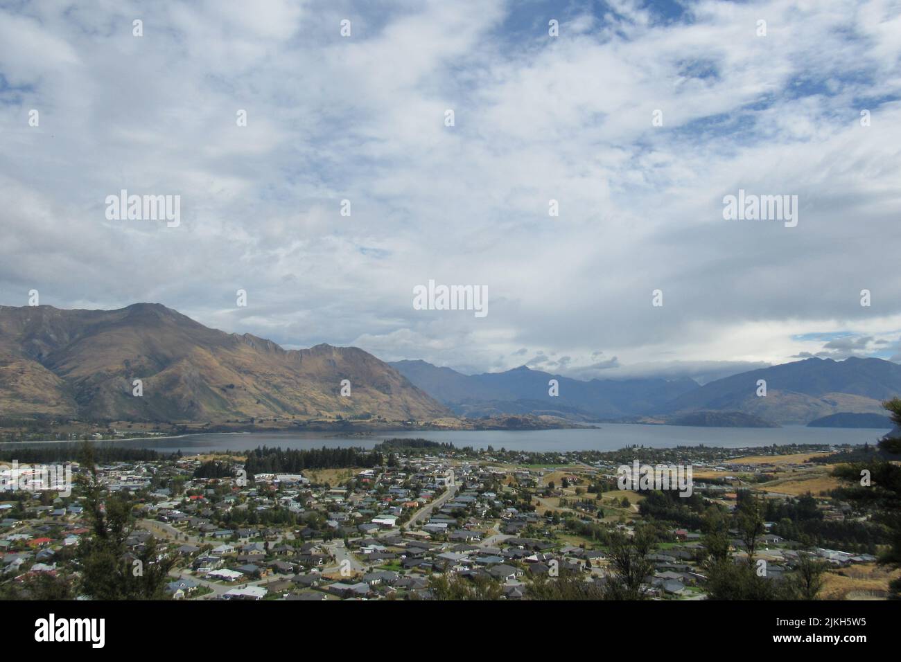 Una vista aerea di un quartiere residenziale contro un lago e montagne in una giornata buia a Wanaka, Nuova Zelanda Foto Stock