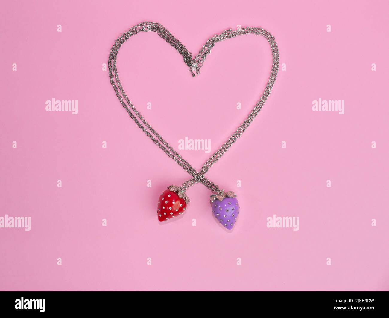 Una collana rossa e una viola fragola a forma di cuore su uno sfondo rosa Foto Stock