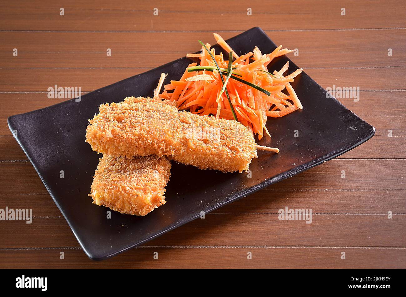 Un bocconcino di pollo si incolla accanto a una carota su un piatto nero Foto Stock