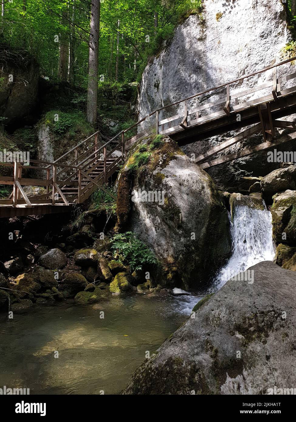 Uno scatto verticale di piccolo ponte di legno sopra il piccolo ruscello che scorre attraverso le rocce ricoperte di muschio Foto Stock