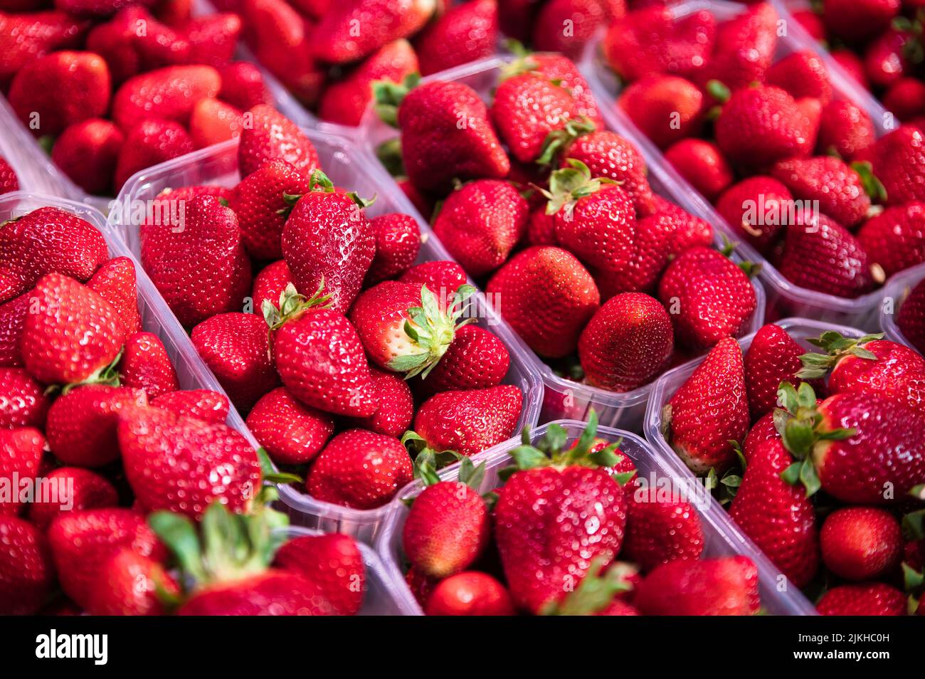 Un primo piano di fragole rosse mature in contenitori di plastica in fila sul mercato di Valencia, Spagna Foto Stock