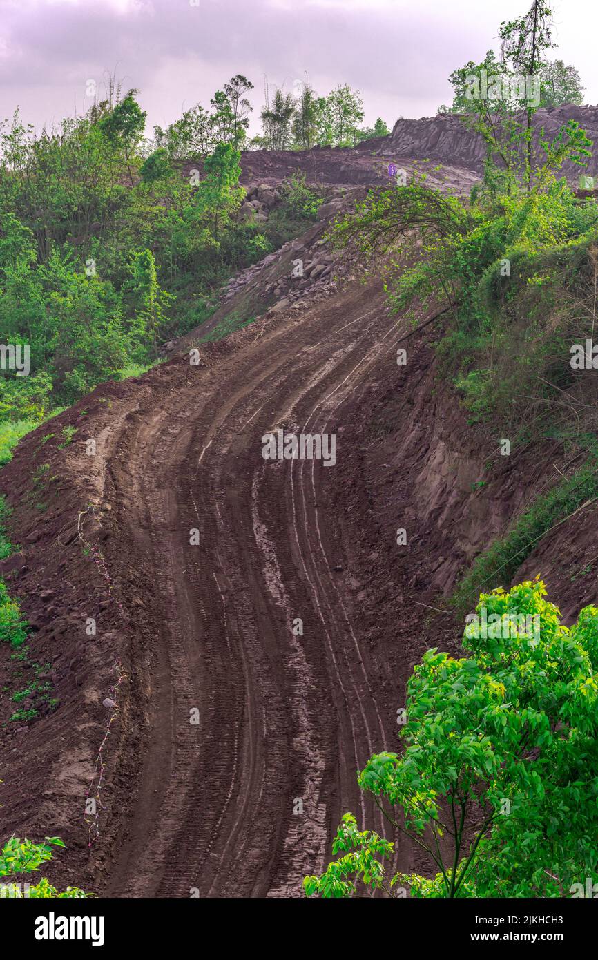 Un colpo verticale di una strada fangosa tra le foreste che si estendono sulla cima della montagna Foto Stock