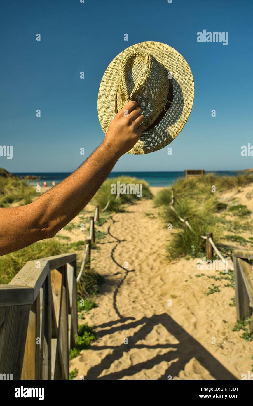 Uomo felice che tiene il cappello fuori su una spiaggia di sabbia con acqua di mare blu turchese sullo sfondo. La gente lifestyle rilassarsi come un viaggiatore in vacanza. Foto Stock Uomo felice che tiene il cappello fuori su una spiaggia di sabbia con acqua di mare blu turchese sullo sfondo. La gente lifestyle rilassarsi come un viaggiatore in vacanza. Foto Stock