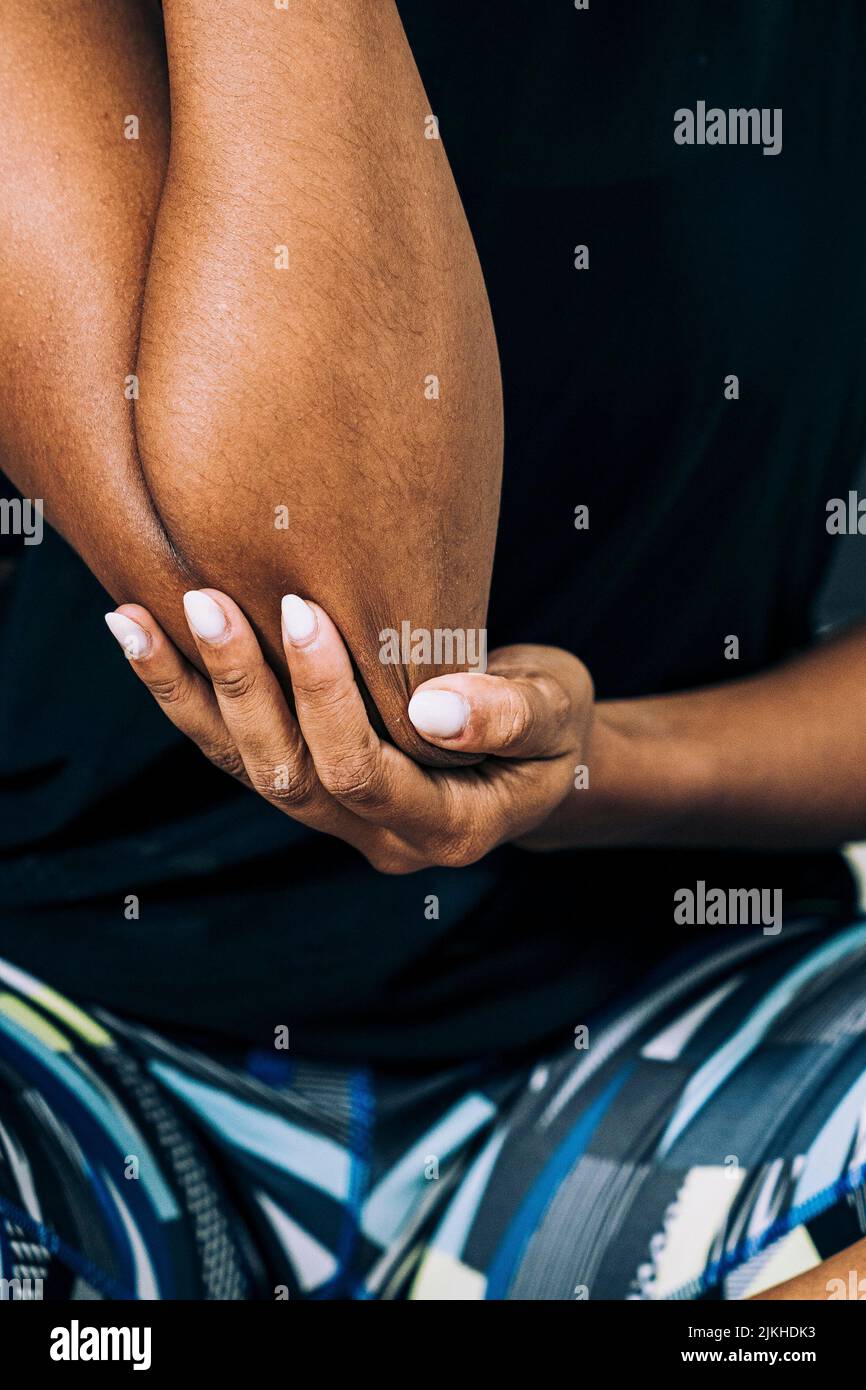 Un primo piano verticale di un'atleta afro-femminile che sfrega il gomito destro nel dolore Foto Stock
