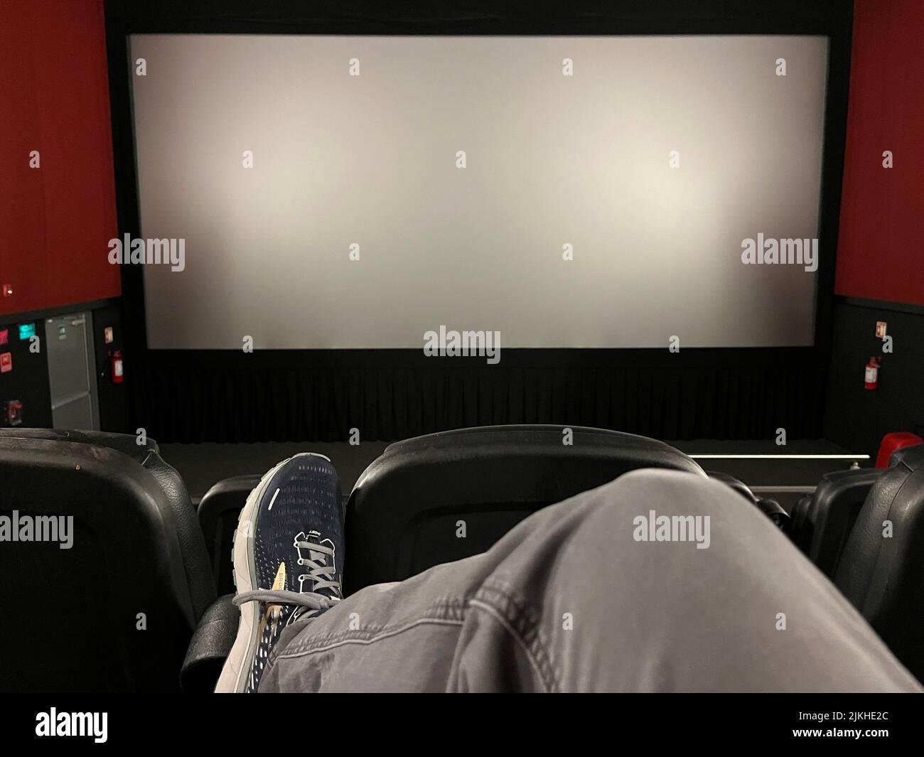 Dal punto di vista di chi guarda un film, vediamo la gamba e la scarpa incrociate mentre si rilassa in un teatro vuoto, guardando uno schermo vuoto fino all'inizio del film Foto Stock