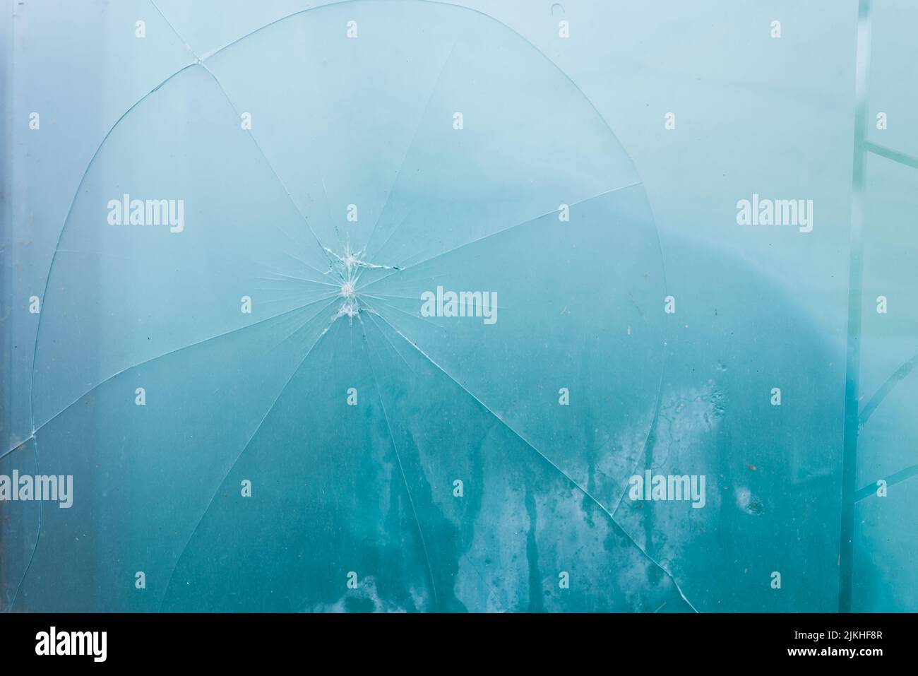 Un primo piano di un vetro rotto fessurato con un foro su sfondo nebbia blu Foto Stock