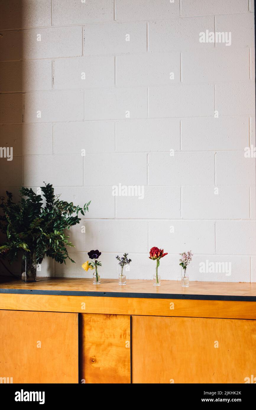 fiori floreali rossi, viola, lilla, gialli in piccole bottiglie di liquore contro muro di mattoni bianchi. spazio copia. Foto Stock