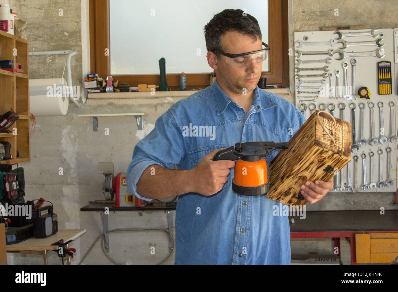 Immagine di un handyman che con una cannella saldatrice brucia e lavora un portabottiglie in legno. Crea il lavoro e lo fai da te Foto Stock