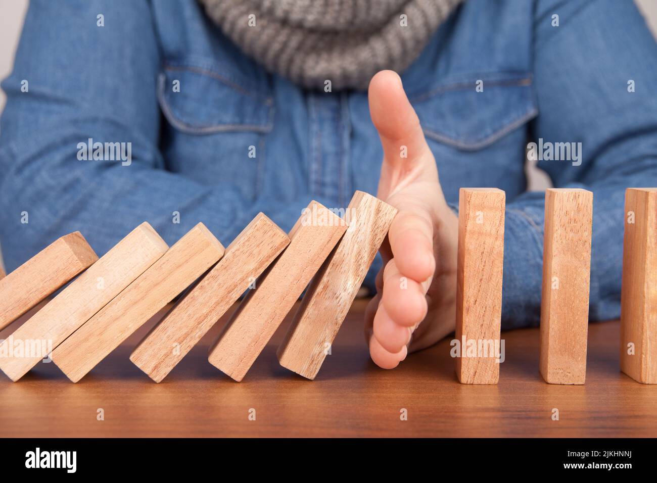 Un primo piano di una mano umana che impedisce ai blocchi di legno di domino di cadere su un tavolo Foto Stock