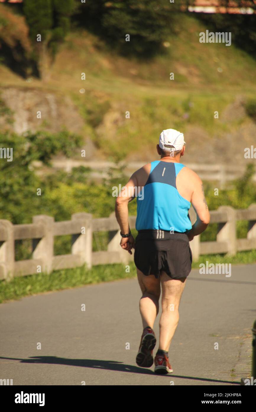 Una vista verticale sul retro di un uomo anziano che fa jogging sulla strada Foto Stock