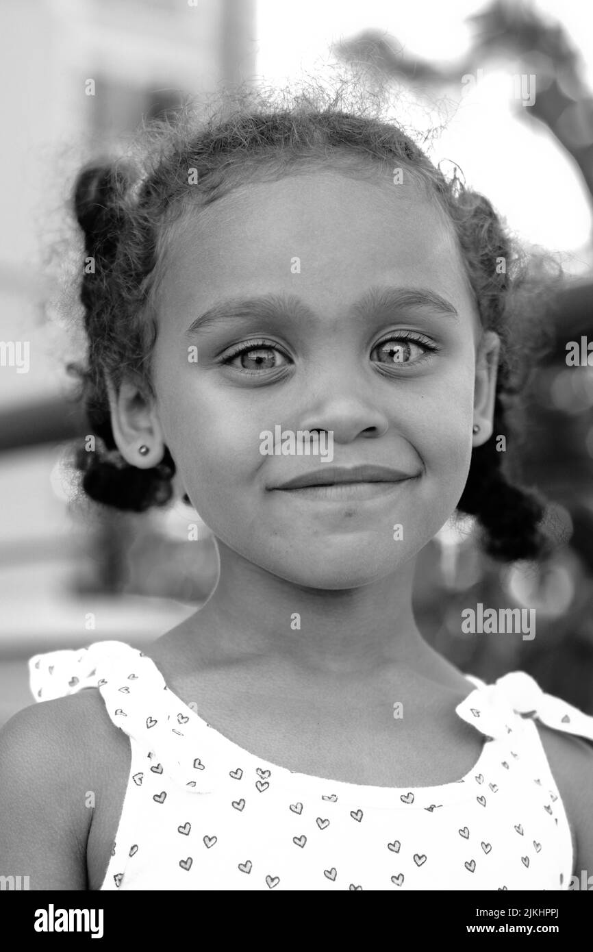 una foto verticale di una bambina sorridente in scala di grigi Foto Stock