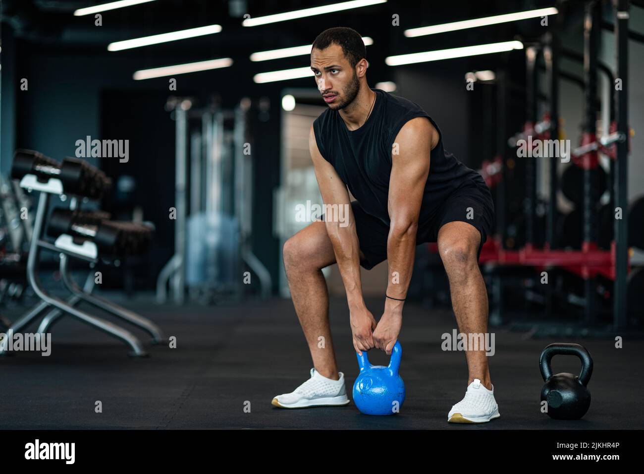 Motivato giovane uomo nero formazione con Kettlebell al moderno Gym Interior Foto Stock