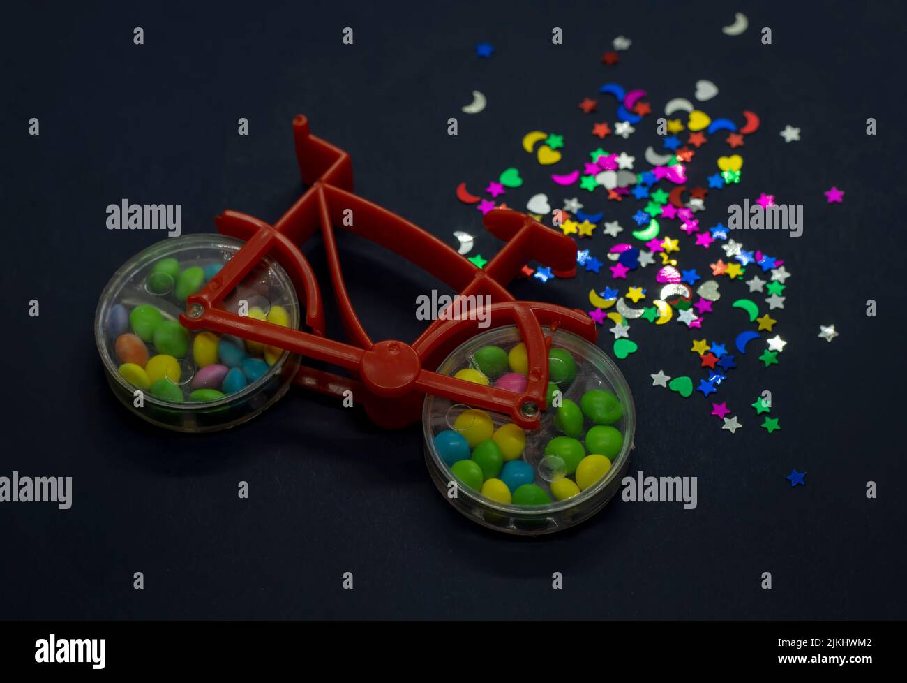 Un primo piano di una bicicletta giocattolo con caramella noce colorata all'interno delle ruote e forme glitterate accanto ad essa Foto Stock