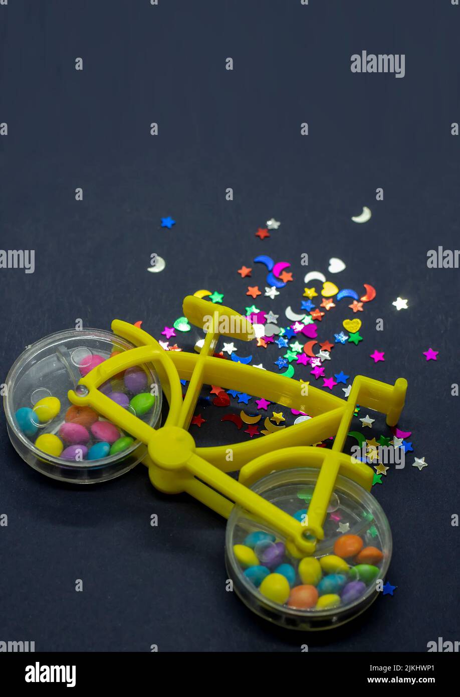 Un primo piano di una bicicletta giocattolo con caramella noce colorata all'interno delle ruote e forme glitterate accanto ad essa Foto Stock