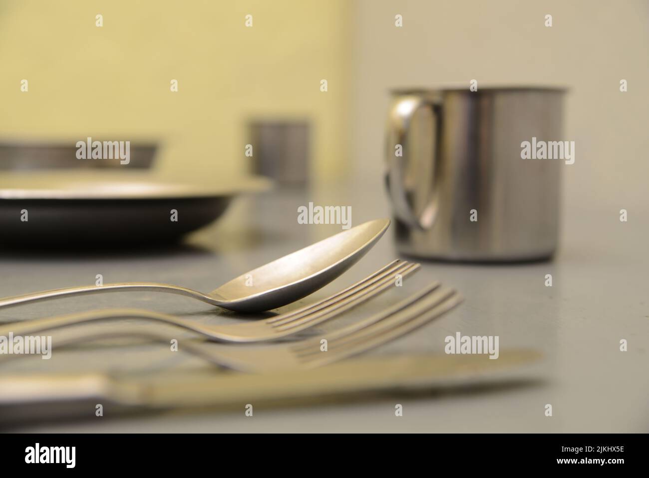 Un primo piano di un cucchiaio e una forchetta con un piatto e una tazza sul tavolo Foto Stock