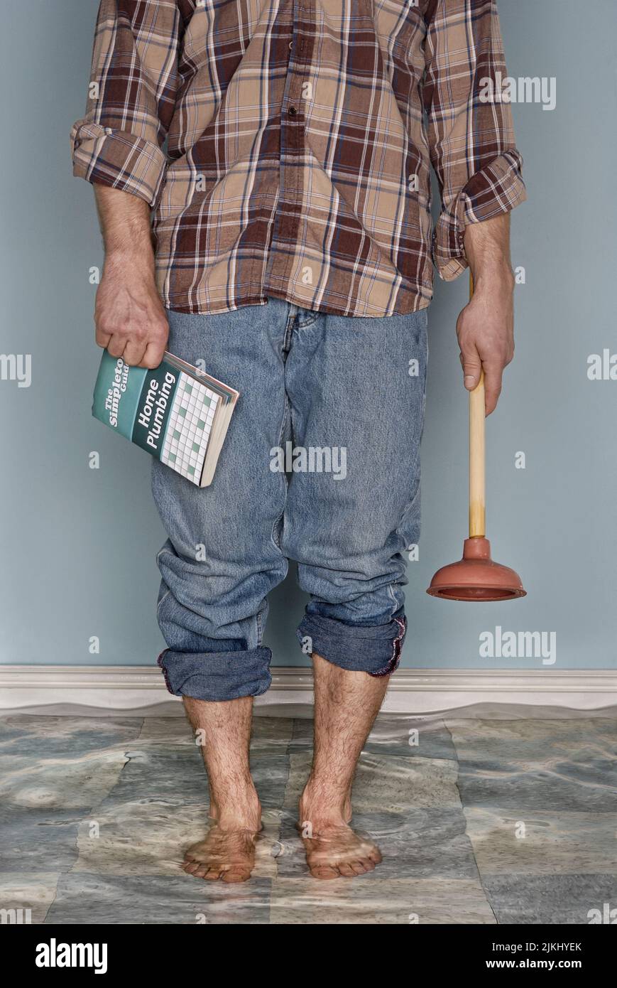 Uno scatto verticale di un maschio in piedi nella stanza riempita di acqua che tiene uno stantuffo e libro circa come riparare il sistema idraulico Foto Stock