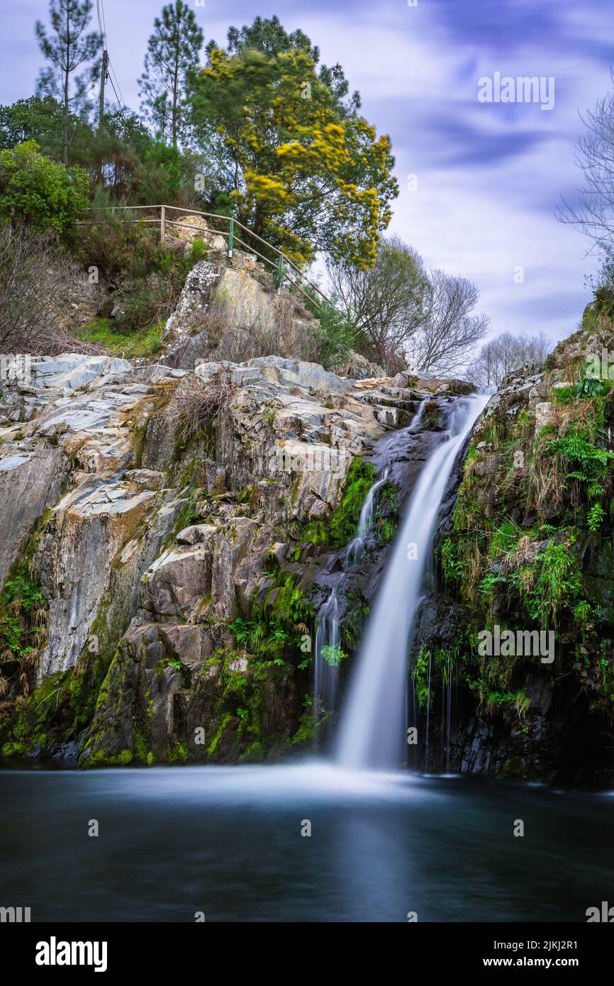 Uno scatto verticale della cascata di Poco da Broca che scorre sulla scogliera di Barriosa, Portogallo Foto Stock