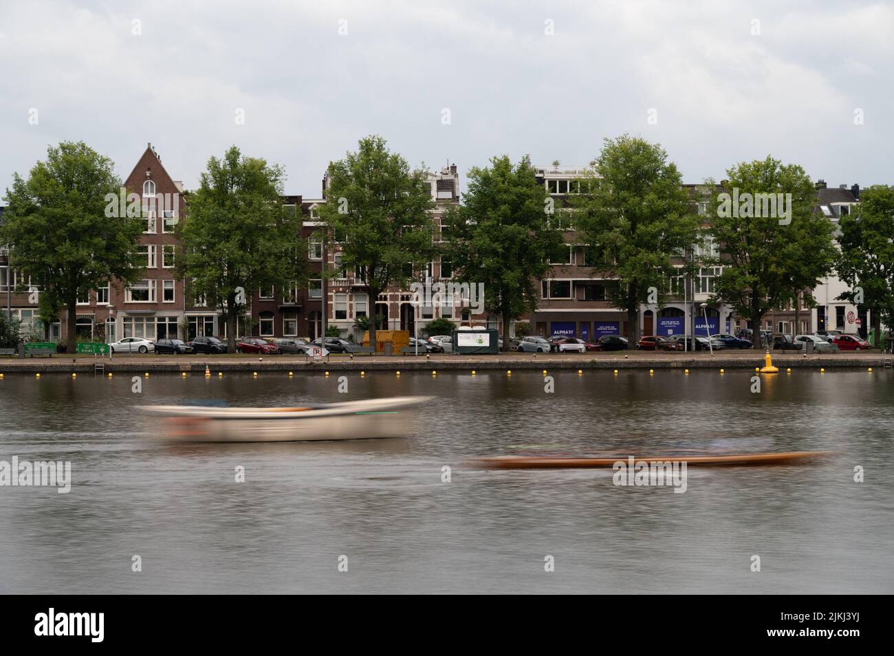 Due barche in rapido movimento che si muovono lungo il fiume Amstel sullo sfondo degli edifici di Amsterdam, nei Paesi Bassi. Foto Stock