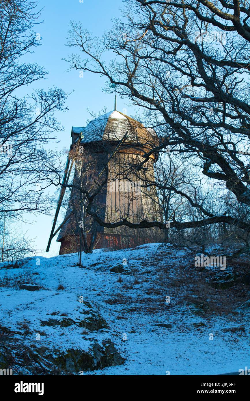 Uno scatto verticale di una giornata innevata a Stoccolma, Svezia, con un mulino a vento circondato da alberi secchi Foto Stock