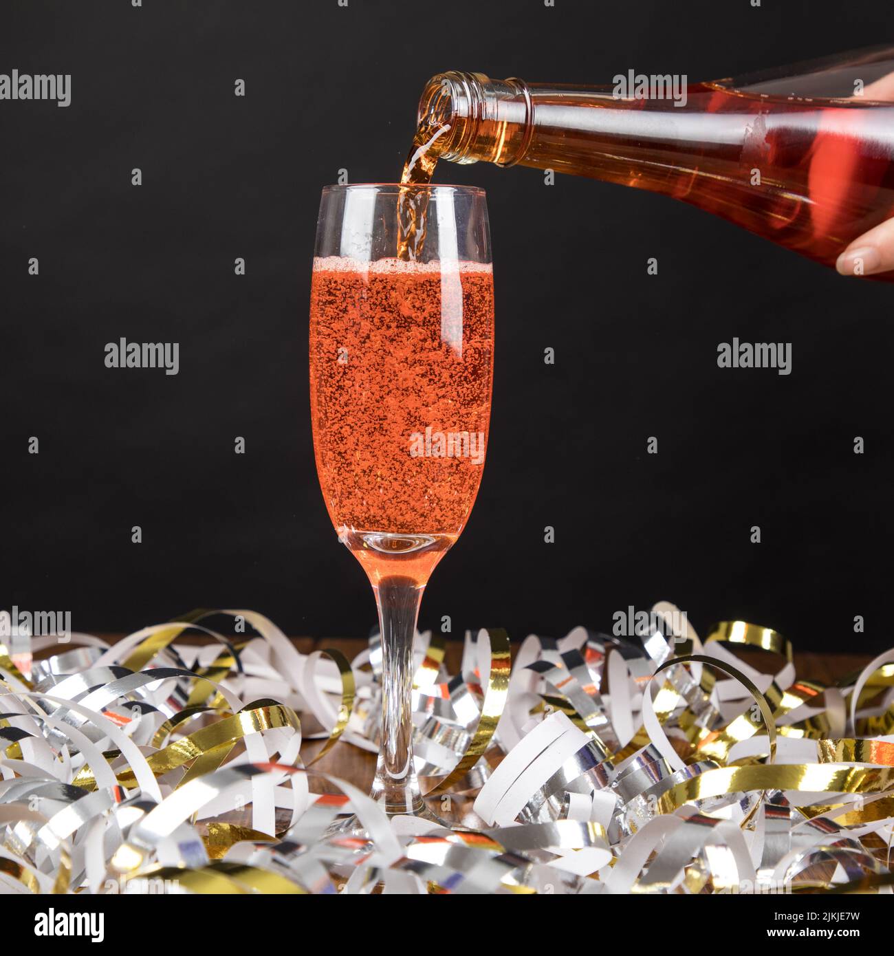 Un primo piano di un bicchiere di champagne rosso con streamer alla festa di Capodanno Foto Stock