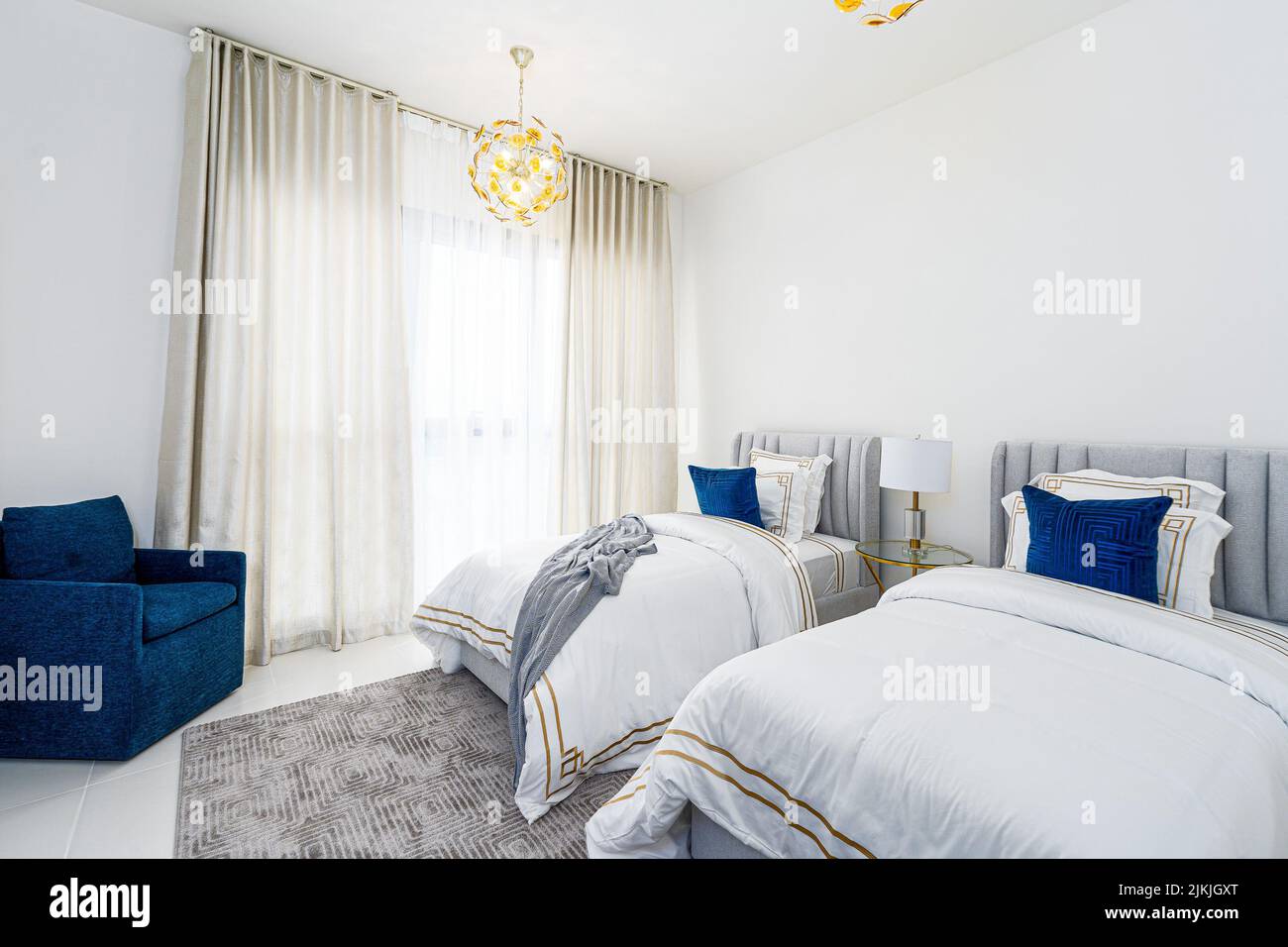 Il moderno design interno degli appartamenti presenta letti grigi, cuscini e una poltrona blu Foto Stock