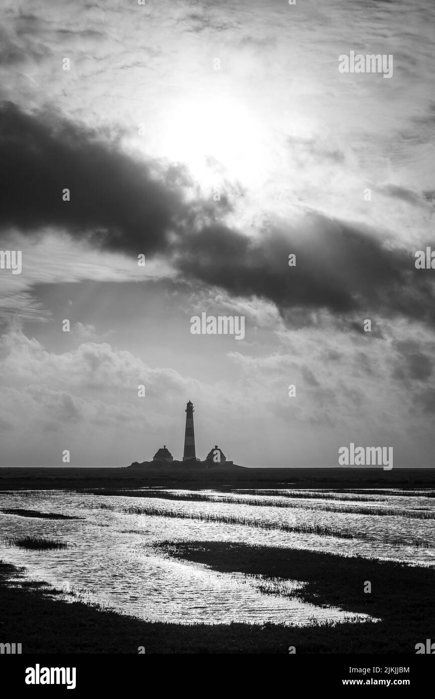 Un'immagine in scala di grigi del faro di Westerheversand nello Schleswig Holstein, in Germania, con un cielo nuvoloso e chiaro Foto Stock
