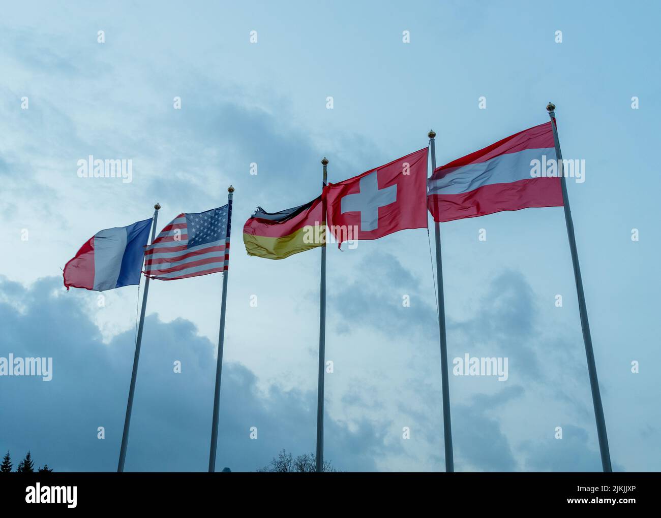 Un colpo d'angolo basso delle bandiere di Francia, USA, Germania, Svizzera e Austria che sbattono su pali metallici contro cielo nuvoloso Foto Stock