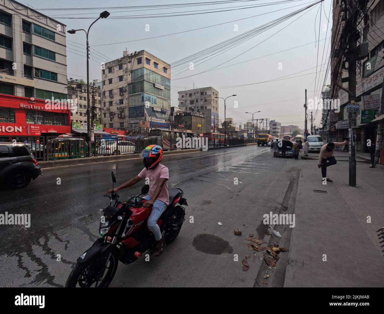 Un motociclista con un casco che corre sulla strada bagnata a Dhaka City persone in Bangladesh Foto Stock