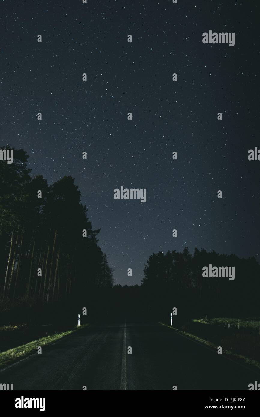 Un colpo verticale della luna splende su una strada solitaria di notte e un cielo stellato Foto Stock