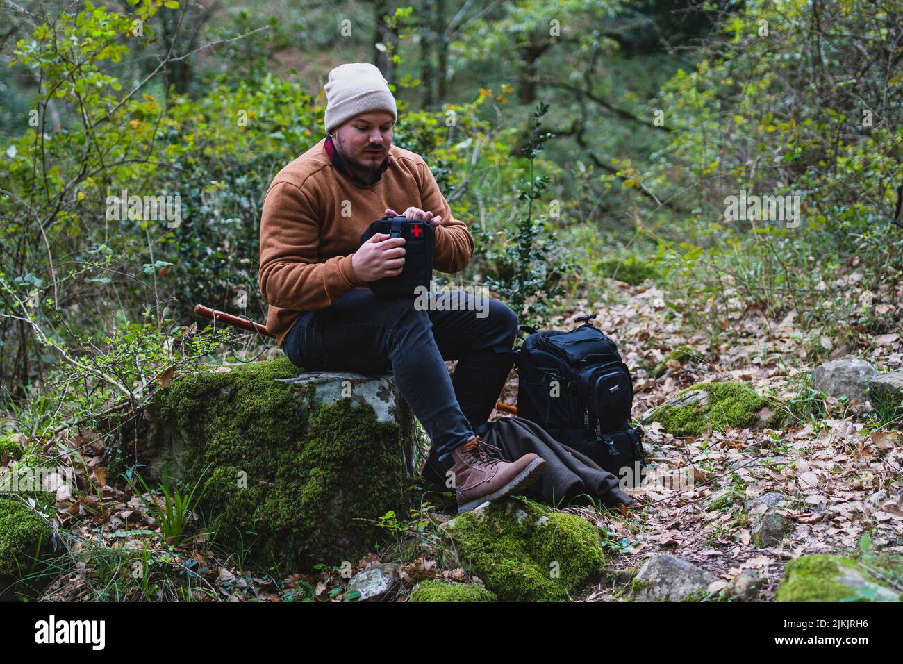 Un uomo caucasico con attrezzature fotografiche professionali seduto su un tronco nella foresta Foto Stock