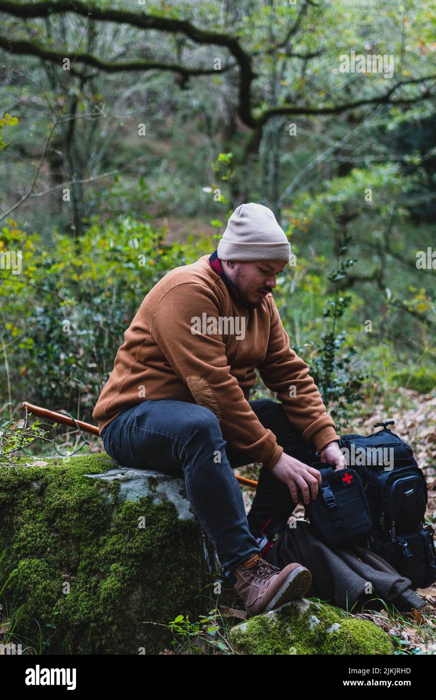 Un colpo verticale di un uomo caucasico con attrezzature fotografiche professionali seduto su un tronco nella foresta Foto Stock