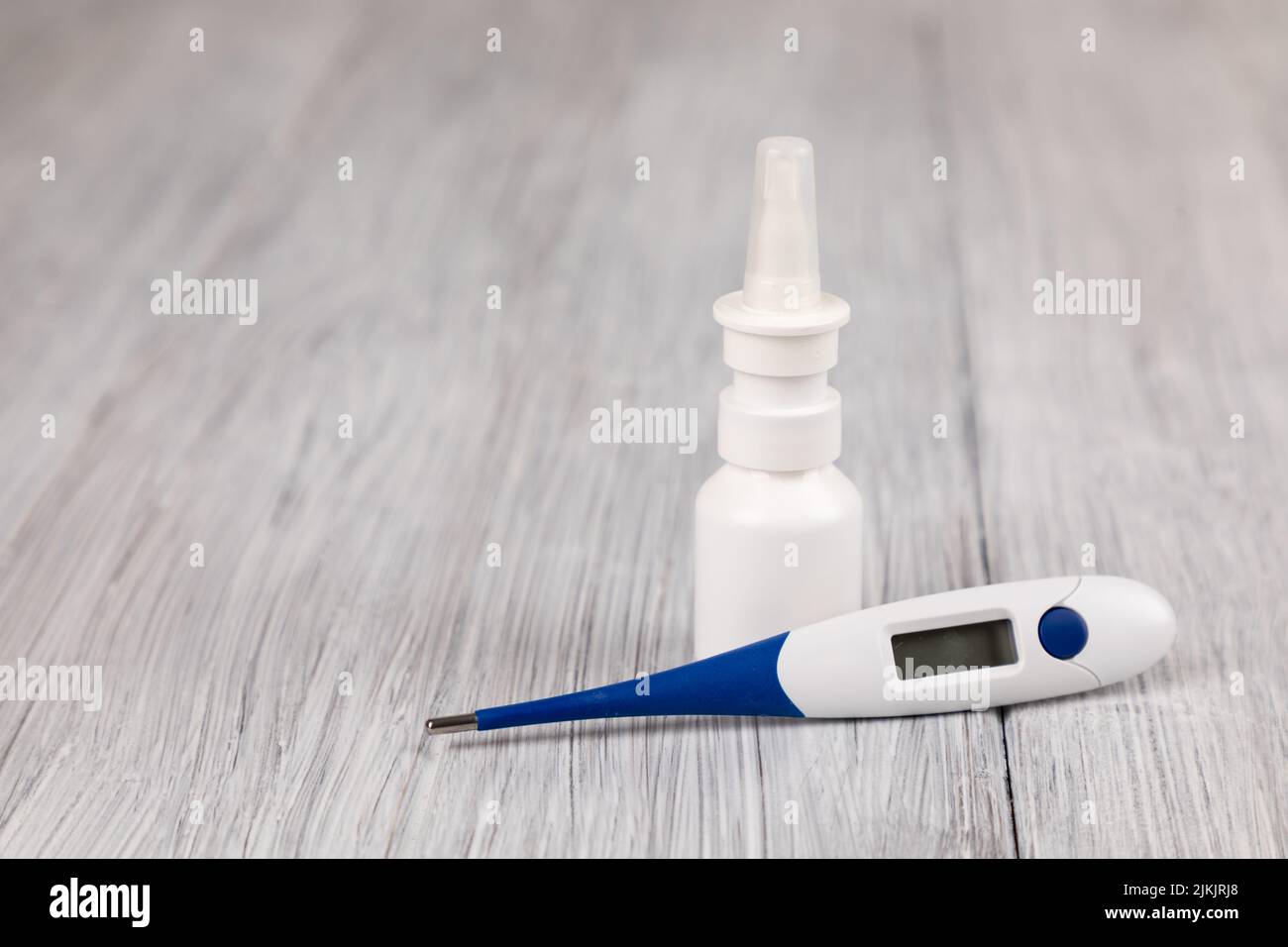 Un primo piano di un termometro e di uno spray nasale su una superficie di legno Foto Stock