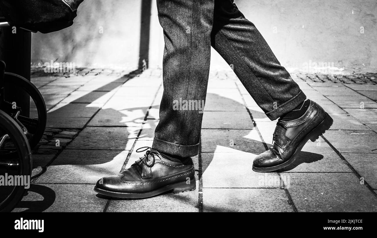 Un primo piano in scala di grigi di un maschio che cammina per strada con scarpe e pantaloni classici Foto Stock