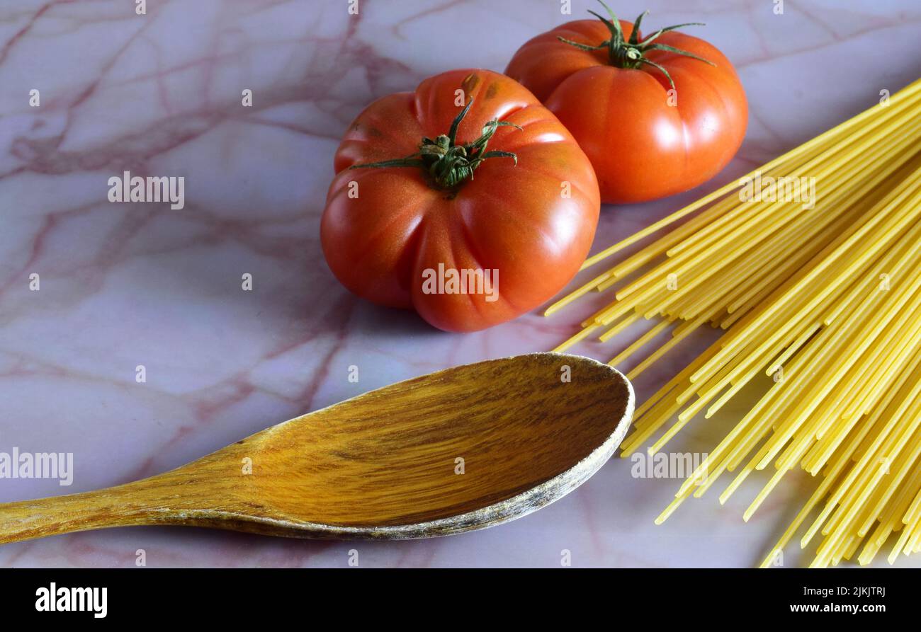 Un primo piano di pomodori con spaghetti non cotti e un cucchiaio di legno sul tavolo. Foto Stock