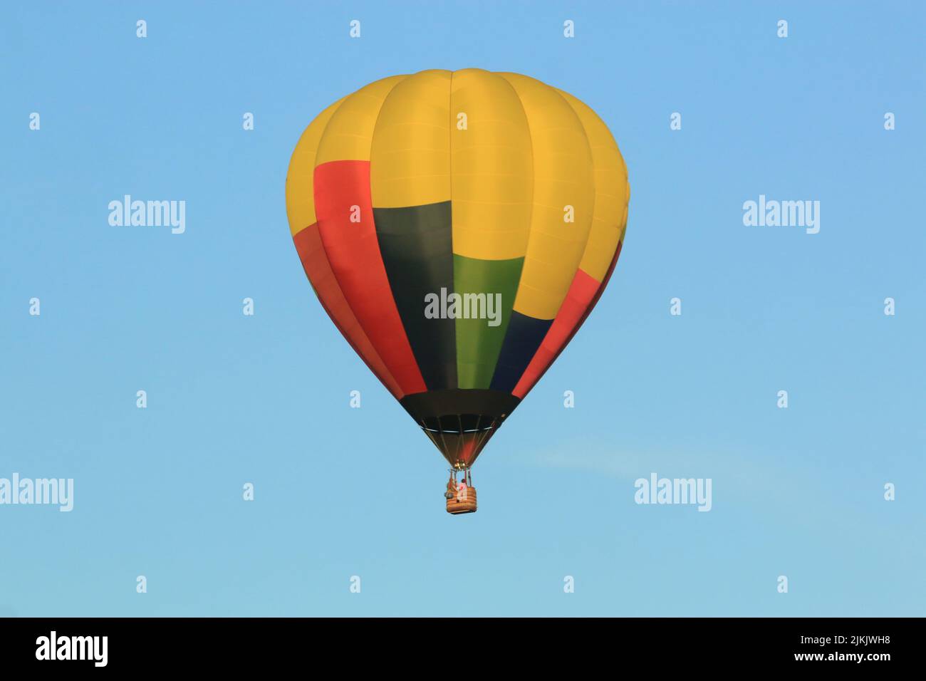 Un primo piano di un colorato pallone ad aria calda che vola in un cielo blu senza nuvole Foto Stock