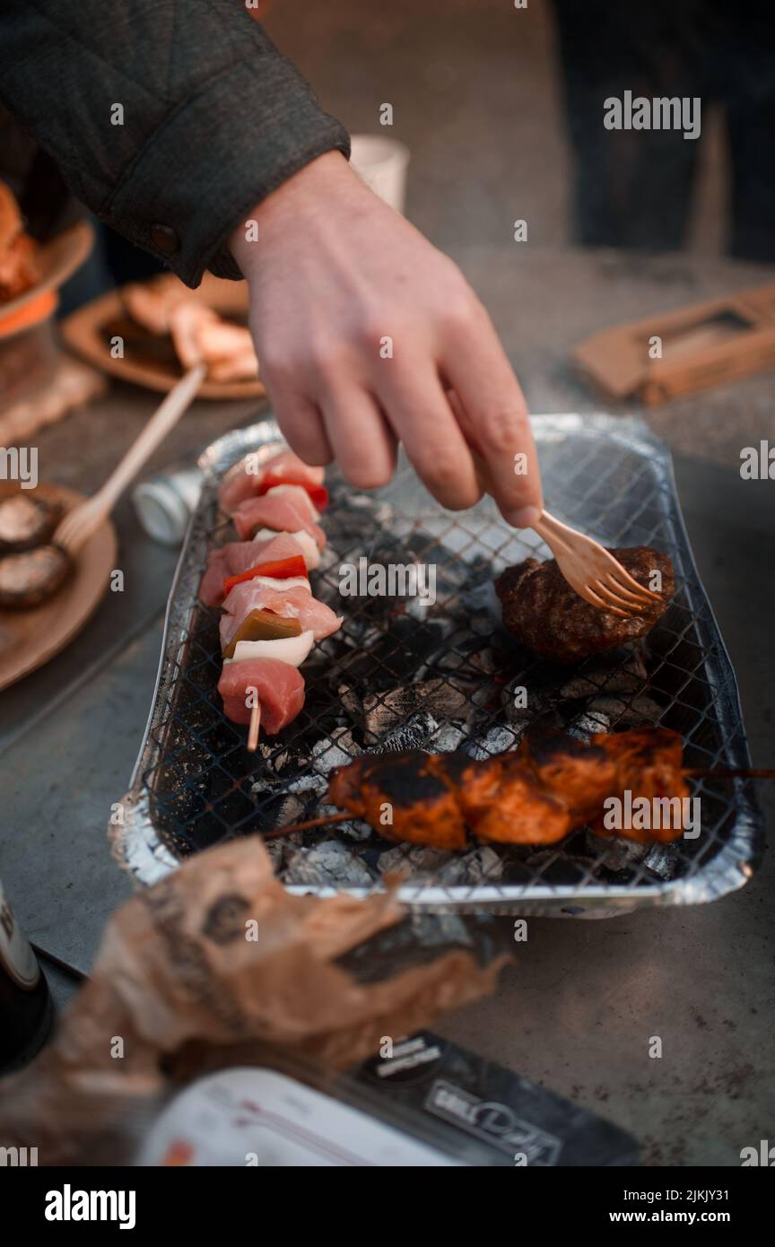 Un colpo verticale di una mano dell'uomo che capovolge la carne sulla griglia con i carboni incandescenti posti su un tavolo Foto Stock