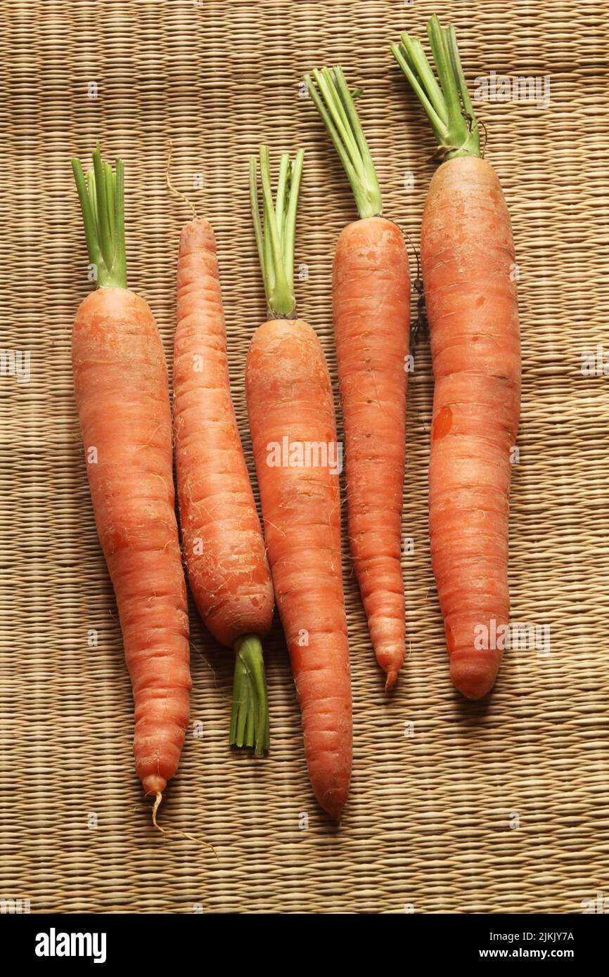 Un colpo verticale di carote arancioni fresche, su una texture marrone vimini Foto Stock