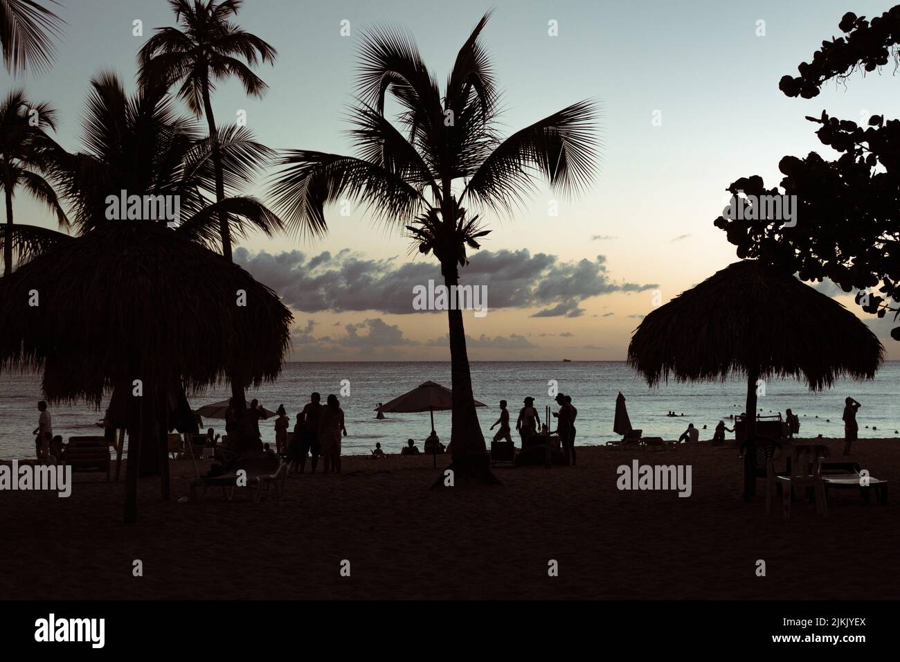 Le sagome delle palme e della gente che riposa sulla spiaggia di Bayahibe al tramonto, Repubblica Dominicana Foto Stock