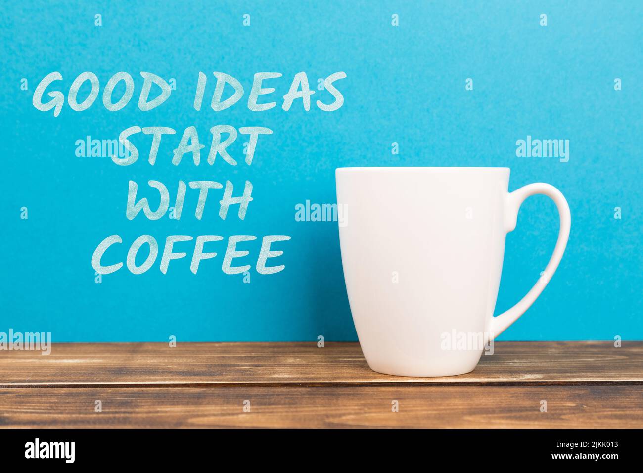 Un primo piano di una tazza bianca con il testo "le buone idee iniziano con il caffè" su sfondo blu Foto Stock