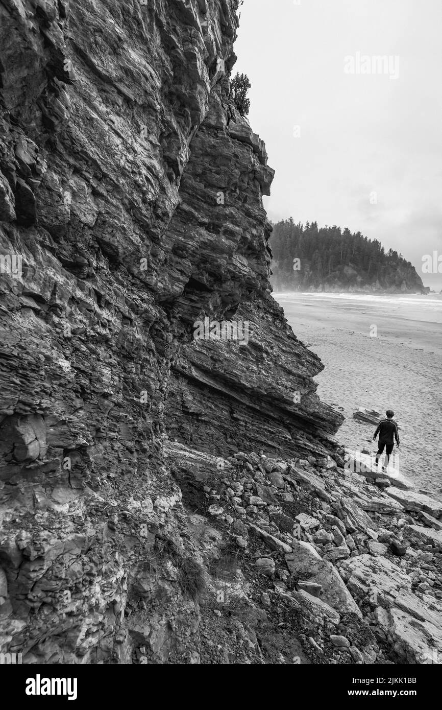 Una puntina bianca e nera raffigurante un uomo in piedi su una spiaggia con una scogliera che lo sostiene Foto Stock