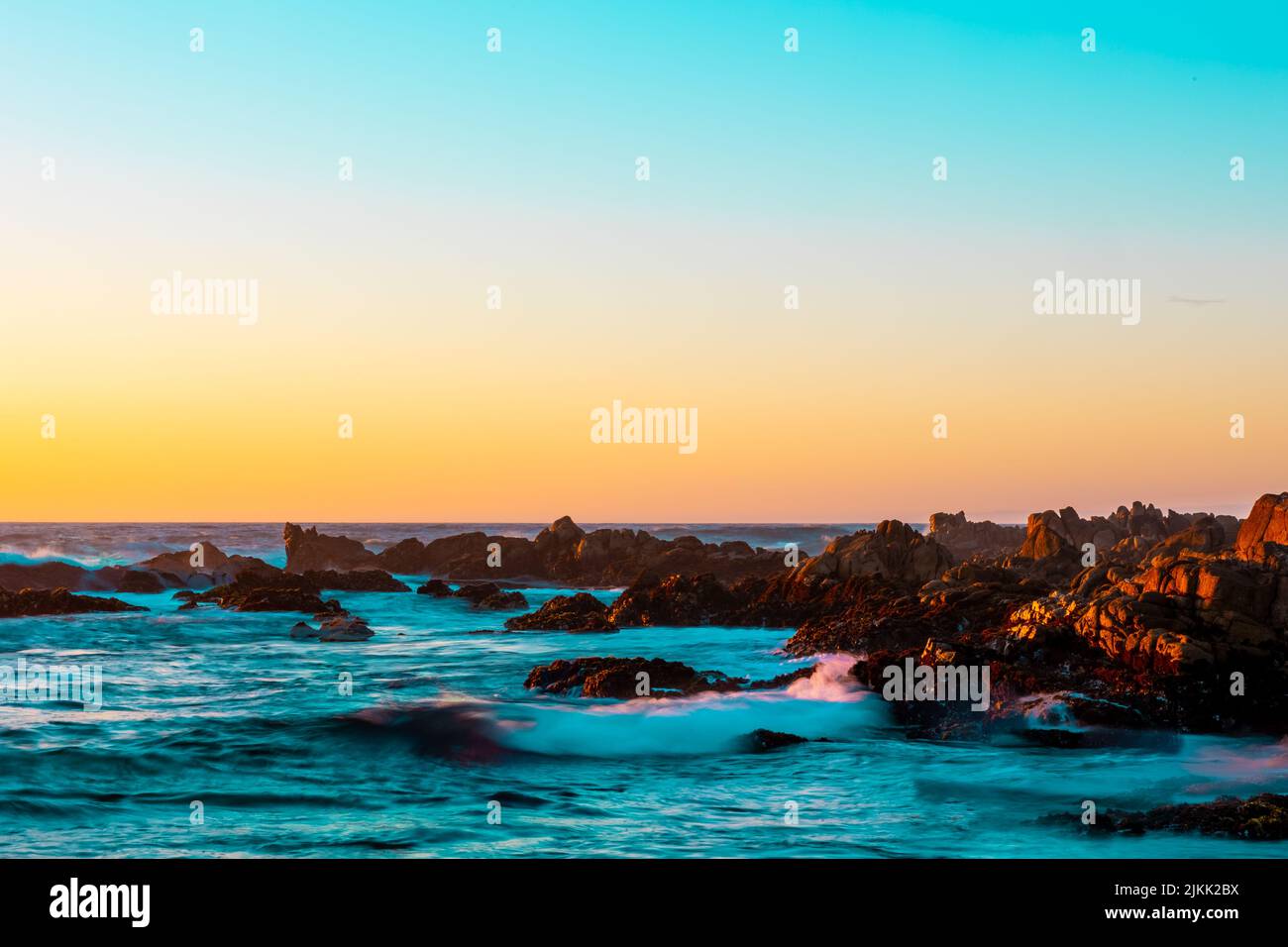 Una vista panoramica dell'oceano, delle rocce e del cielo dai colori caldi durante il tramonto Foto Stock