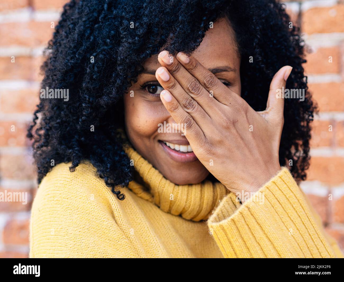 Una donna africana dalla Spagna in un maglione giallo che copre il suo volto con una mano Foto Stock Una donna africana dalla Spagna in un maglione giallo che copre il suo volto con una mano Foto Stock