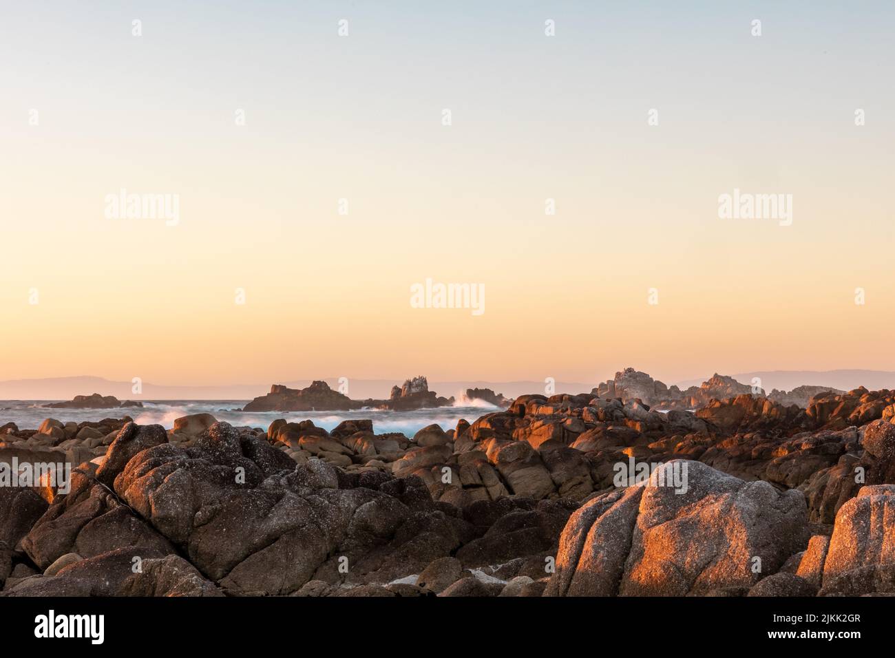 Una vista panoramica dell'oceano con molte rocce di fronte e un cielo dai colori caldi Foto Stock