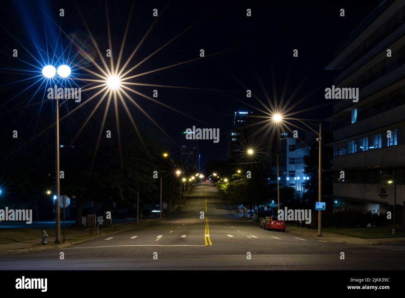 Una bella foto di una strada vuota con auto parcheggiate e luci di strada di notte in Arkansas, Stati Uniti Foto Stock