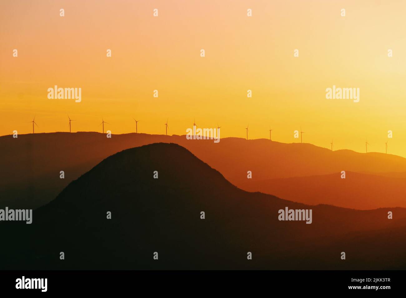 Una silhouette di un tempo nebbia sulle montagne durante il tramonto con mulini a vento in cima Foto Stock