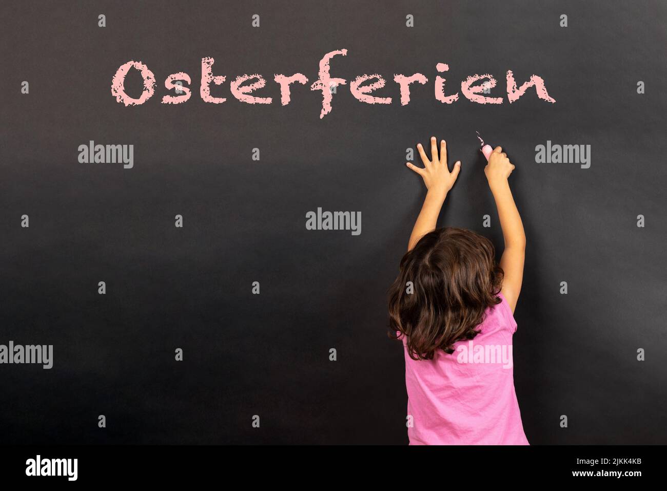 Ragazza che scrive su una lavagna il testo tedesco Osterferien, in inglese pasqua vacanze Foto Stock