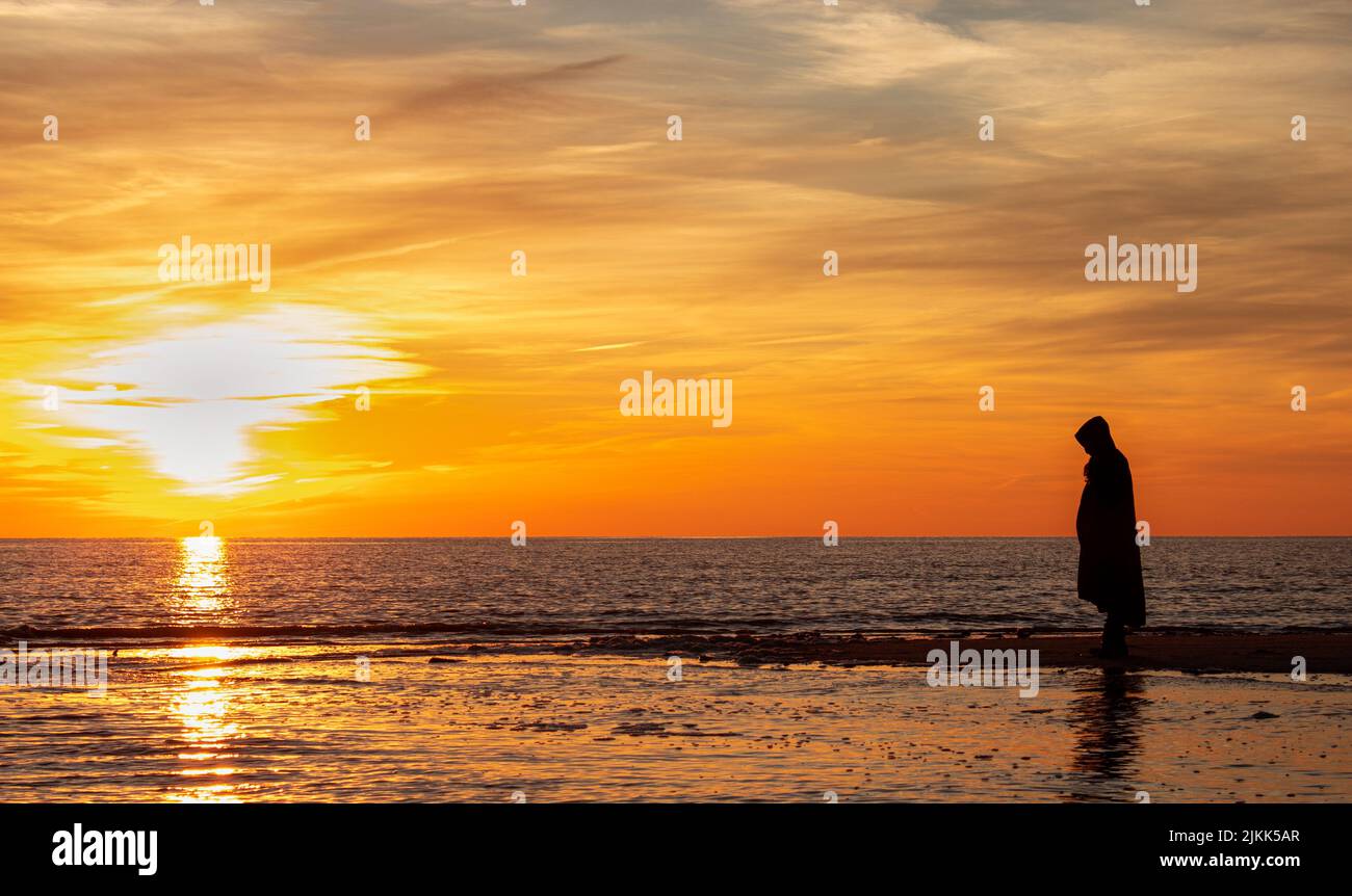 Una silhouette di un uomo in un mantello nero sulla riva al tramonto Foto Stock